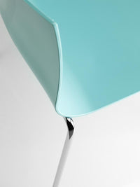 Detalle de la silla de restaurante Slim italiana, con asiento celeste de borde curvo y unión a una pata cromada